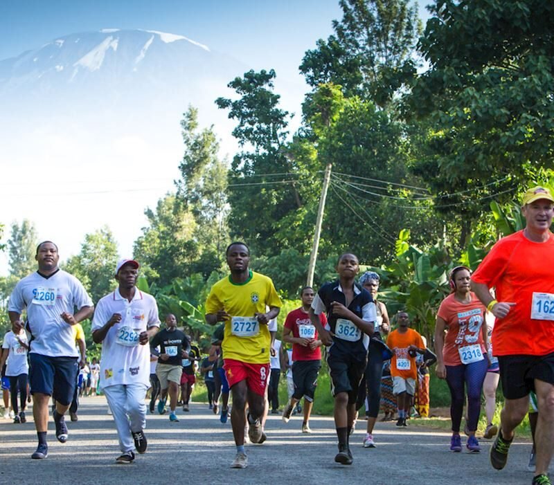 Runners participating in the Kili Marathon with Mount Kilimanjaro in the background. The image captures a vibrant and dynamic scene of the marathon event, showcasing participants in athletic gear, the majestic snow-capped peak of Kilimanjaro, and the scenic landscape of Tanzania. Ideal for highlighting adventure sports, marathon events, and travel experiences in Africa.